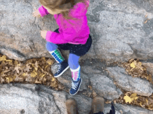 a little girl in a pink jacket and blue socks is climbing up a rock