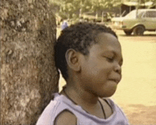 a young boy leaning against a tree with his eyes closed and a car in the background .