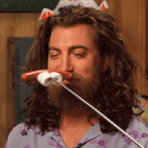 a man with long hair and a beard is eating a hot dog from a stick