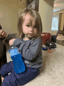 a little girl is sitting on the floor holding a bottle of water