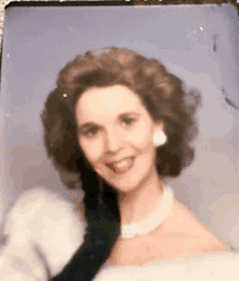 a woman wearing a white dress and a black glove is smiling for the camera .