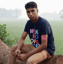 a young man is sitting on a log wearing a shirt that says week bd one de