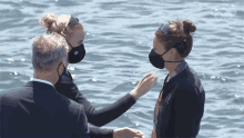 a man and two women wearing face masks are standing in the water with the olympic rings in the background