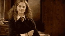 hermione granger is wearing a black sweater and a red tie and smiling .