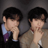two young men in suits and ties are standing next to each other and covering their mouths with their hands .
