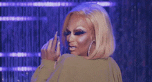 a drag queen is making a funny face while standing on a stage in front of a purple background .