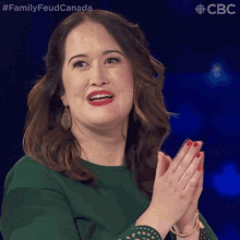 a woman in a green dress is clapping her hands in front of a blue background that says family feud canada