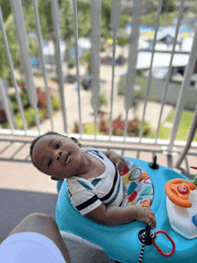 a baby is laying in a blue walker on a balcony looking at the camera