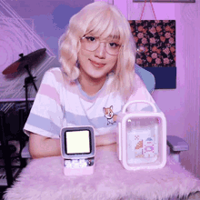 a woman wearing glasses and a striped shirt is sitting at a table holding a pink box and a smaller box