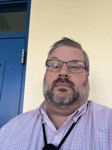 a man with glasses and a beard is making a funny face in front of a blue door