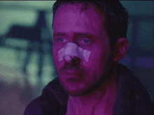 a man with a bandage on his nose is looking at the camera in a purple light .