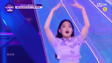 a girl in a purple shirt is dancing on a stage with her hands in the air .