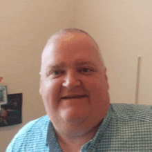 a man in a blue and white checkered shirt is smiling for the camera .