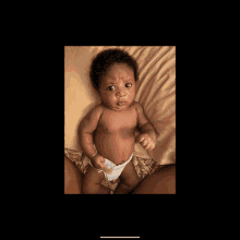 a baby in a diaper laying on a bed looking at the camera