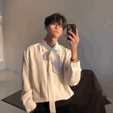 a man in a white shirt taking a selfie with his phone