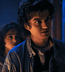 a close up of a man 's face with a woman behind him in a dark room