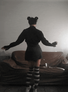 a woman in a black skirt and striped knee high socks stands in front of a couch