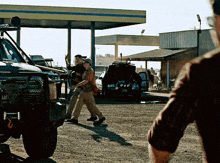 a man in a brown shirt stands in front of a jeep with a license plate that starts with the letter l