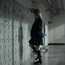 a girl leans against a wall of lockers in a hallway with a green sign that says 2 on it