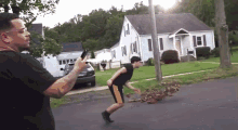 a man in a black shirt is holding a gun while a man in a black shirt is running down the street