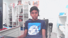 a boy wearing a blue shirt that says great world sits in a chair