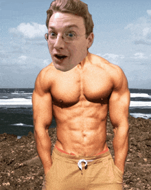 a shirtless man with glasses is standing on a rocky beach with his hands in his pockets