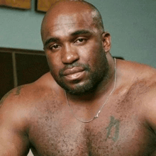 a shirtless man with a tattoo on his chest is wearing a necklace and looking at the camera .