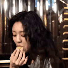 a woman with long black hair is eating a piece of food in front of a sign that says welcome