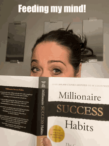 a woman holds a book titled millionaire success habits in front of her face