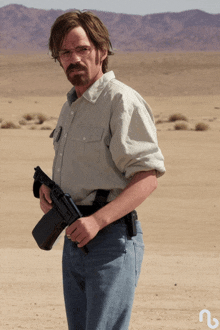 a man with glasses and a beard holds a gun in a desert