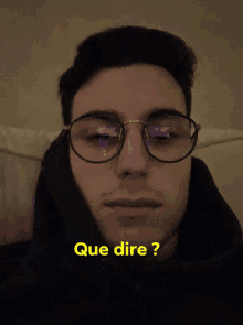 a man wearing glasses and a black hoodie with que dire written in yellow