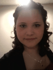 a young woman with curly hair is taking a selfie with a light shining on her face .