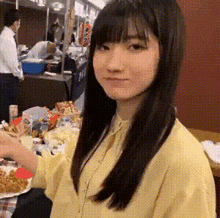 a young woman in a yellow shirt is sitting at a table with a plate of food in front of her .