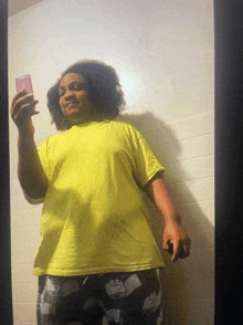 a person in a yellow shirt is taking a selfie with a pink phone