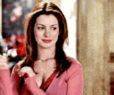 a woman wearing a pink sweater and a necklace looks at the camera