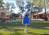a person in a blue dress and white hat is standing in a park