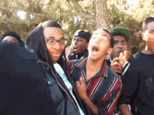 a group of young men are standing in a park and one of them is wearing glasses and a hoodie