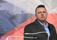 a man in a suit and blue shirt stands in front of a flag