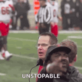 a group of men are watching a football game and one of them is wearing a hat and glasses .