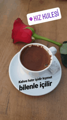 a cup of coffee sits on a saucer next to a red rose and a sign that says " kiz kulesi "