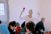 a group of young men are dancing in a room while a man holds a rose .