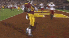 a football player in a maroon uniform is holding a football in his hand while standing on a field .