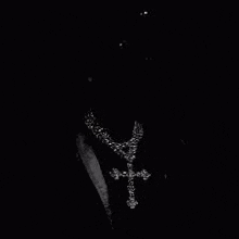 a black and white photo of a man wearing a necklace with a cross pendant .