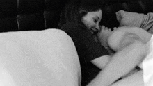 a black and white photo of a woman kissing a man 's foot while laying on a bed .