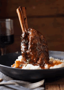 a black plate topped with mashed potatoes and meat with a glass of wine behind it