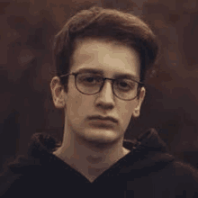 a young man wearing glasses and a black hoodie looks at the camera .