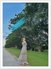 a woman stands in front of a row of trees and a sign that says " sunday "