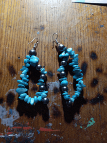 a pair of earrings made of turquoise and black beads on a wooden table