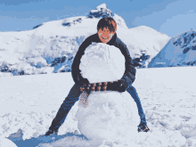 a man is making a snowman in the snow with a mountain in the background and a watermark that says fwdfwdfwd