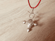 a silver pendant on a red string on a wooden table